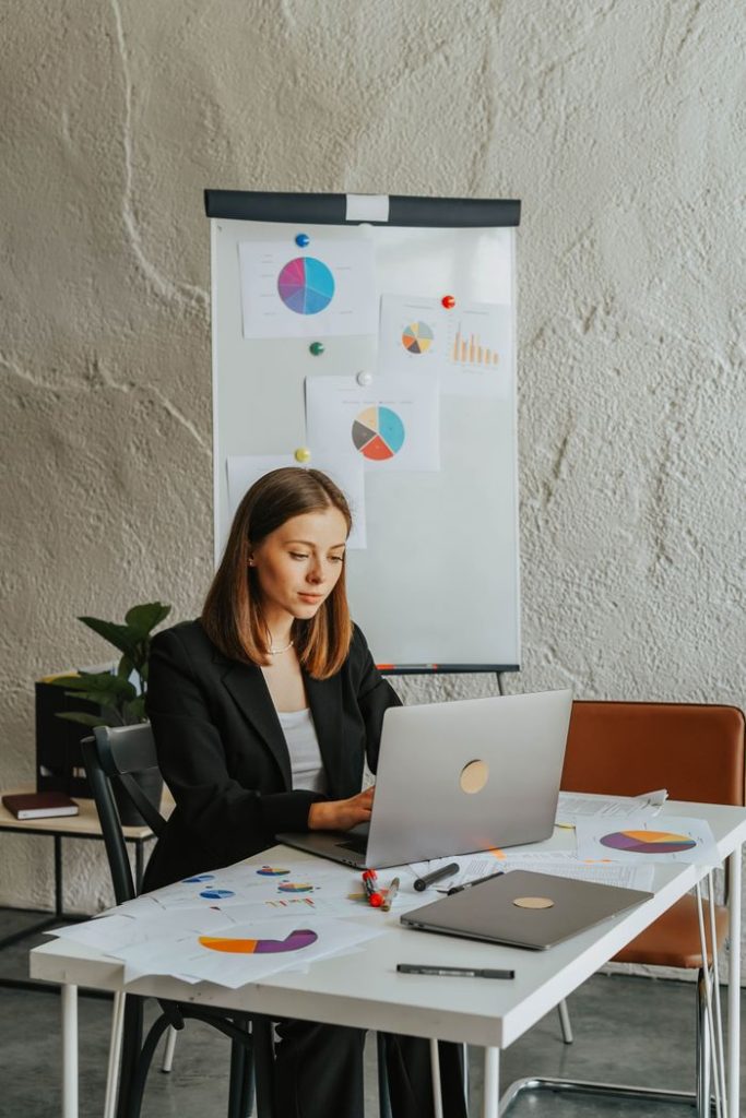 Professional woman in blazer analyzing charts and graphs on laptop in modern office setting.